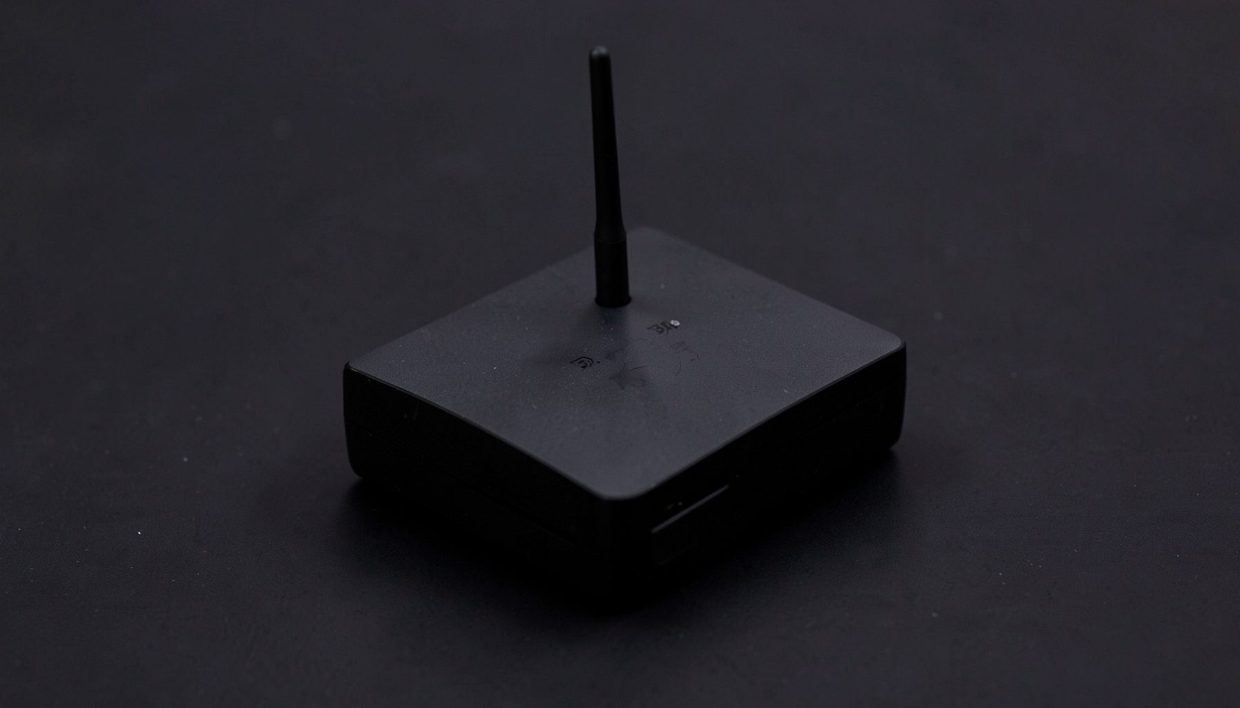 Crni Android TV Box uređaj kvadratnog oblika s antenom, na tamnoj podlozi
